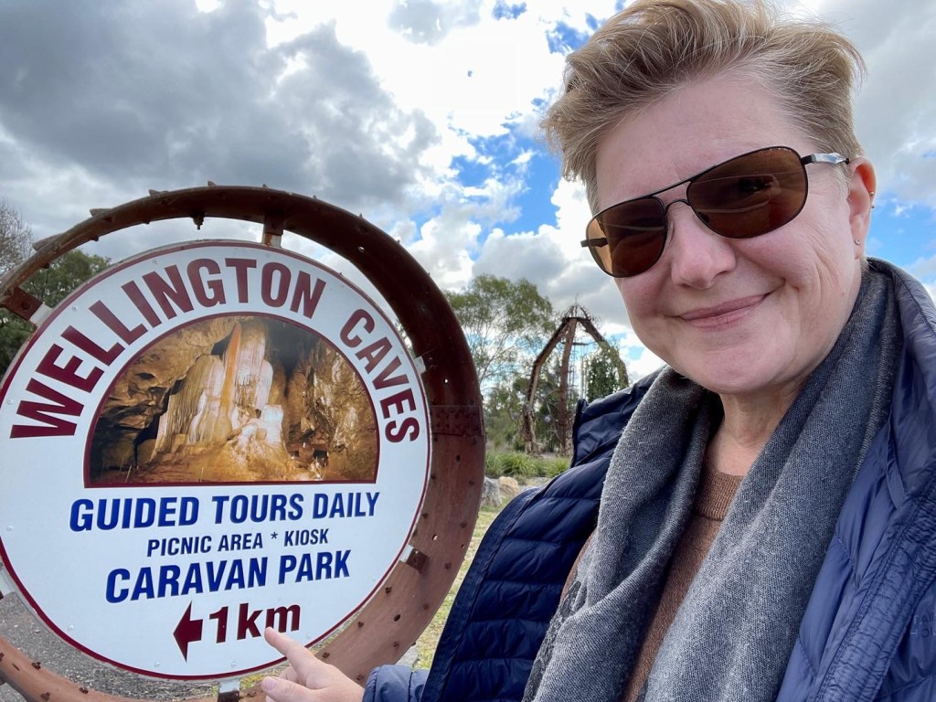 Artist Kim V. Goldsmith pointing to a sign for Wellington Caves